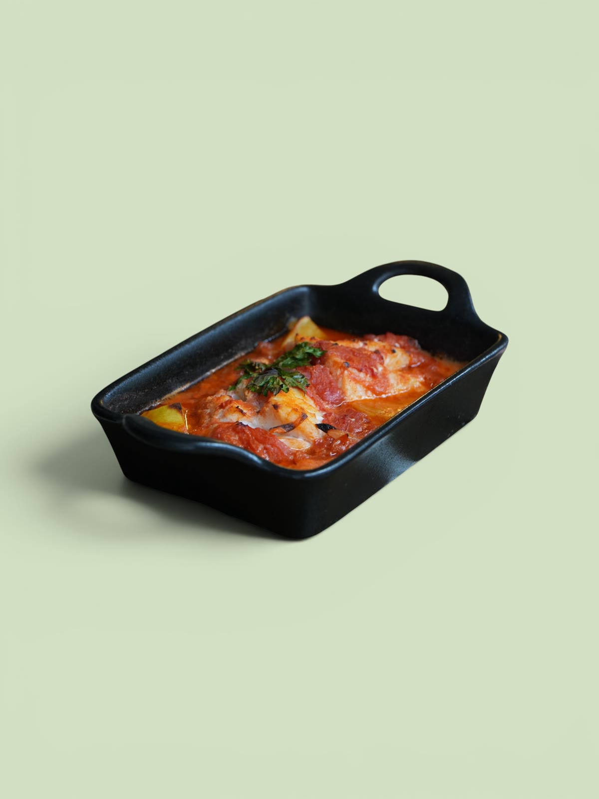Baked dish in a black pan on a green background, packshot for A Tavola